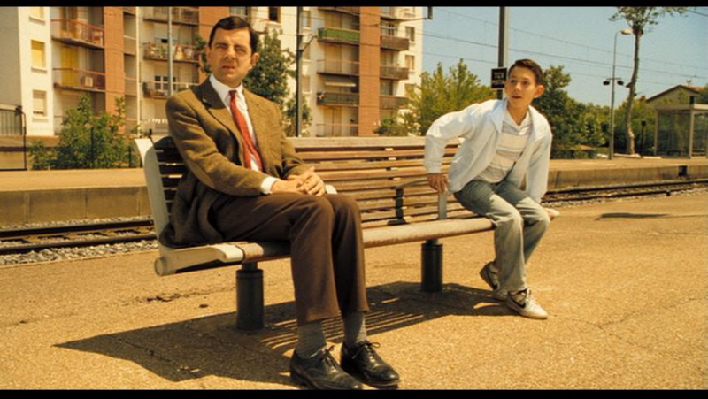 Film Mr. Beans Holiday sitzt auf einer Wartebank am Bahnhof